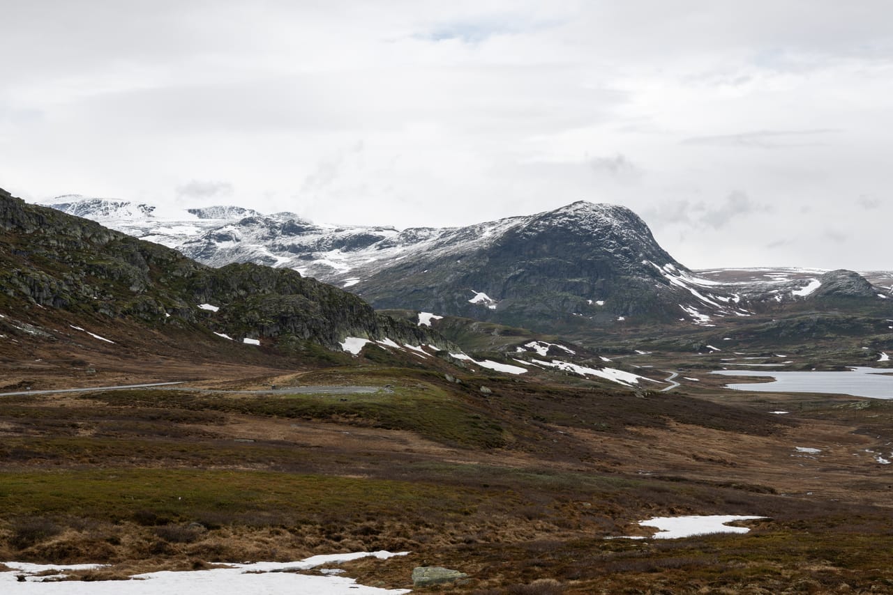 Valdresflye på vei mot Bygdin, med snøflekker i heiene og en liten innsjø i det fjerne.