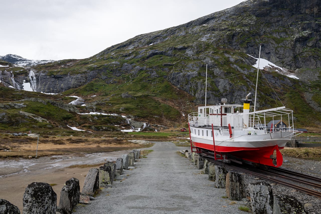 MB Bitihorn på slippen ved Bygdin, med et bratt fjellparti og smeltevannsfosser i bakgrunnen.
