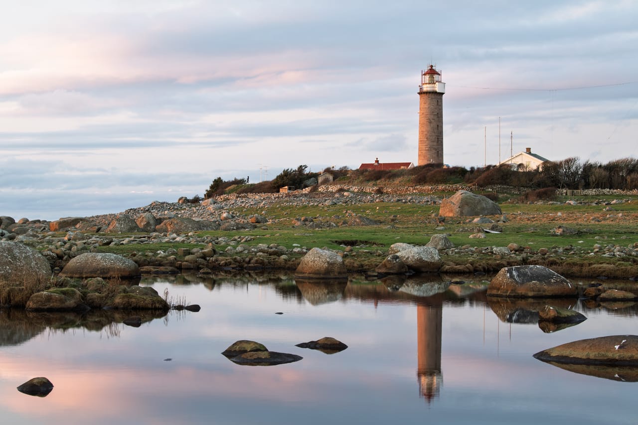 Lista fyr sett over Vågen, med fyrtårnet speilet i vannflaten og et fargerikt skydekke over.