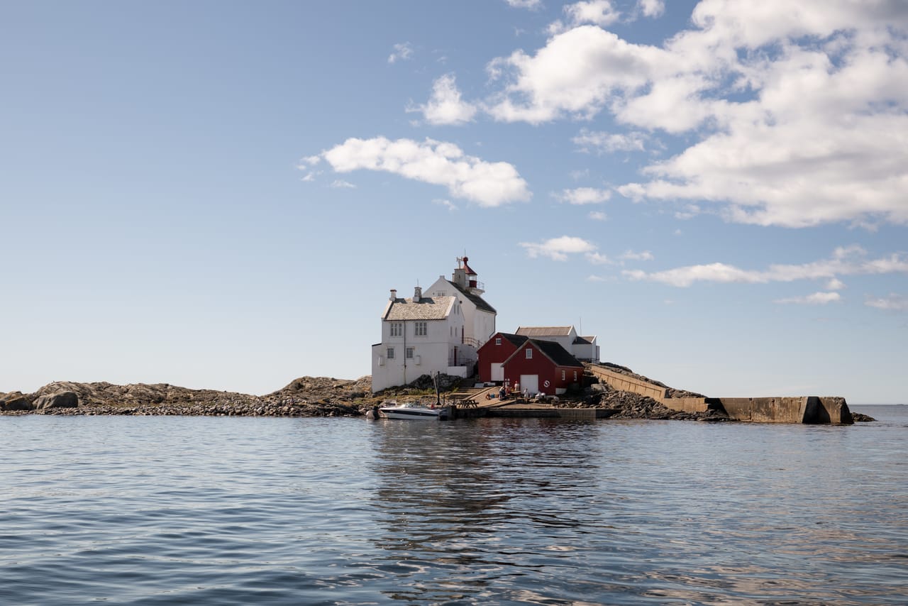 Grønningen fyr på nærmere hold, med hvitmalt fyrbygning og rødt naust på svaberget.