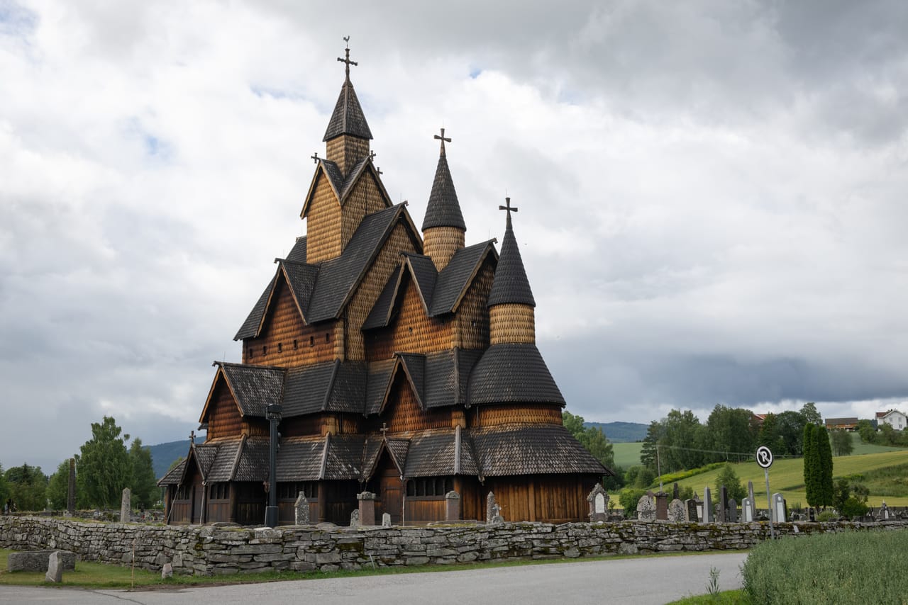 Heddal stavkirke i overskyet vær, med de karakteristiske tårnene og steinmuren rundt kirkegården.
