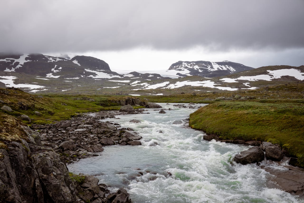 Elv som renner gjennom steinete terreng, med Hardangerjøkulen skimtet i bakgrunnen.