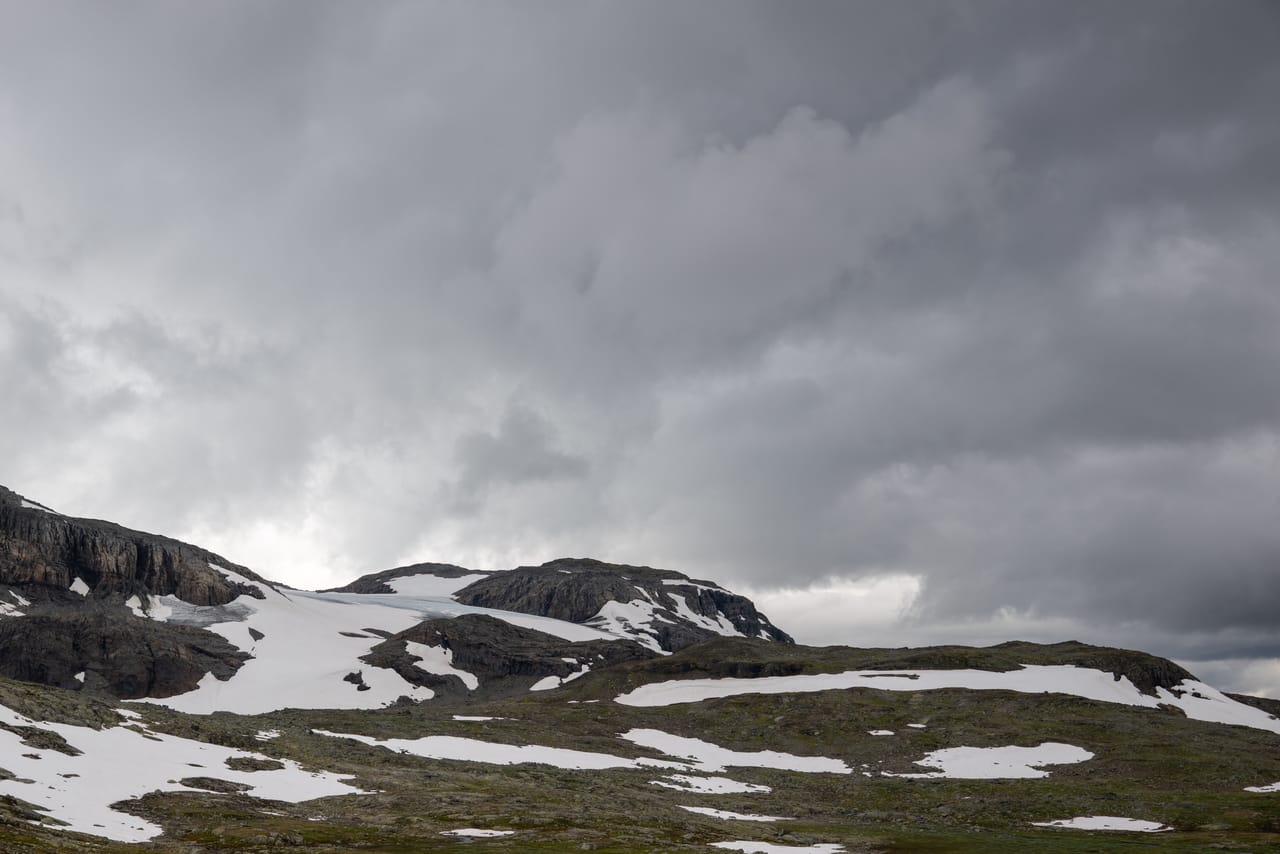 Snødekket fjellrygg med kanten av en isbre synlig mellom skyene.