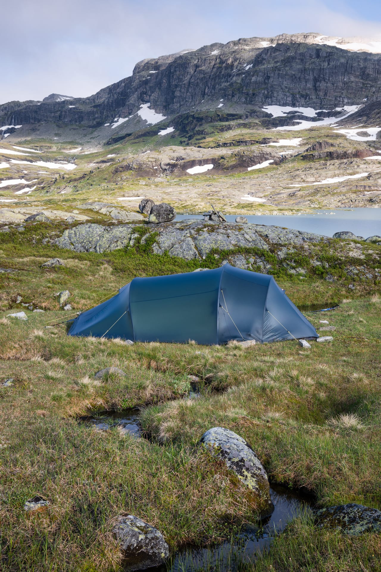 Telt ved et fjellvann i kveldslys, med et bratt fjellparti i bakgrunnen.