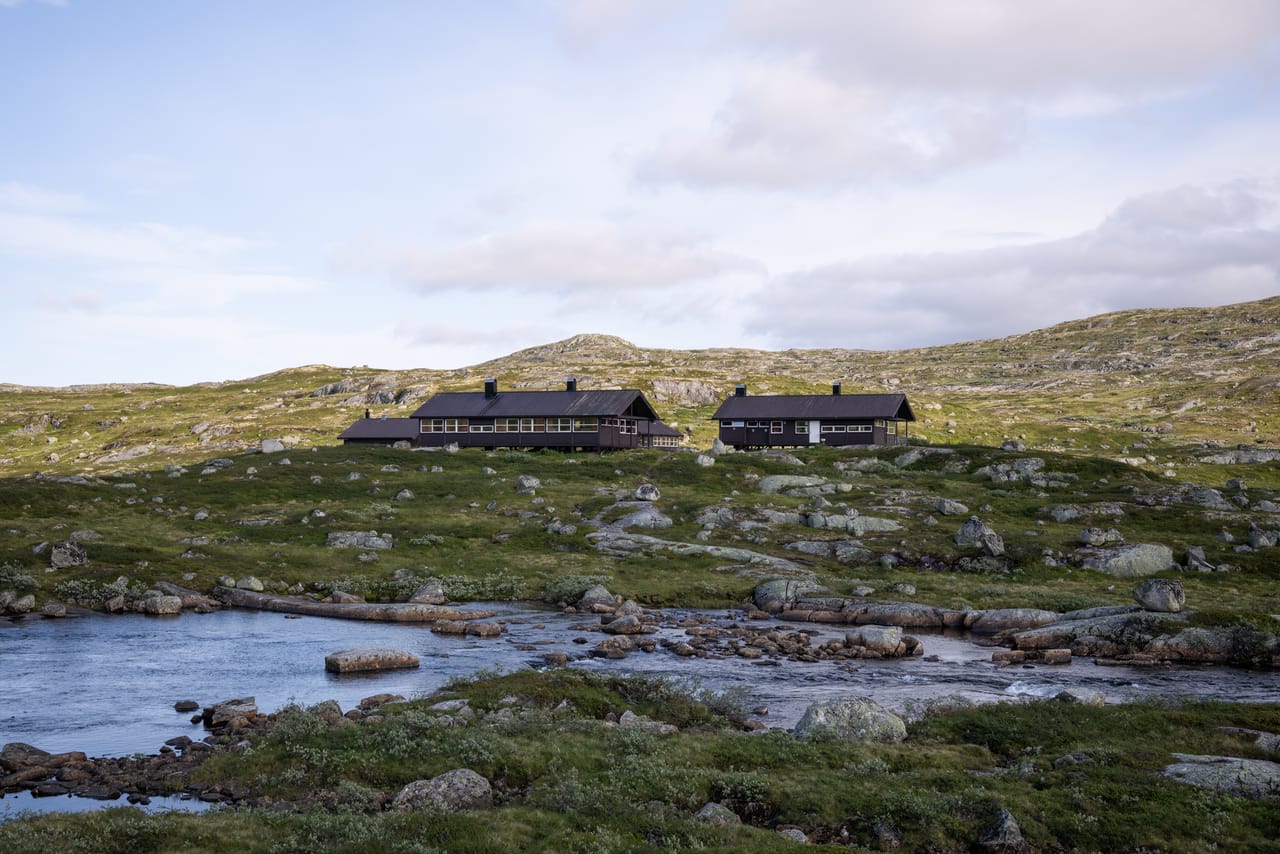 Kjeldebu turisthytte sett fra elvebredden, i kveldslys.