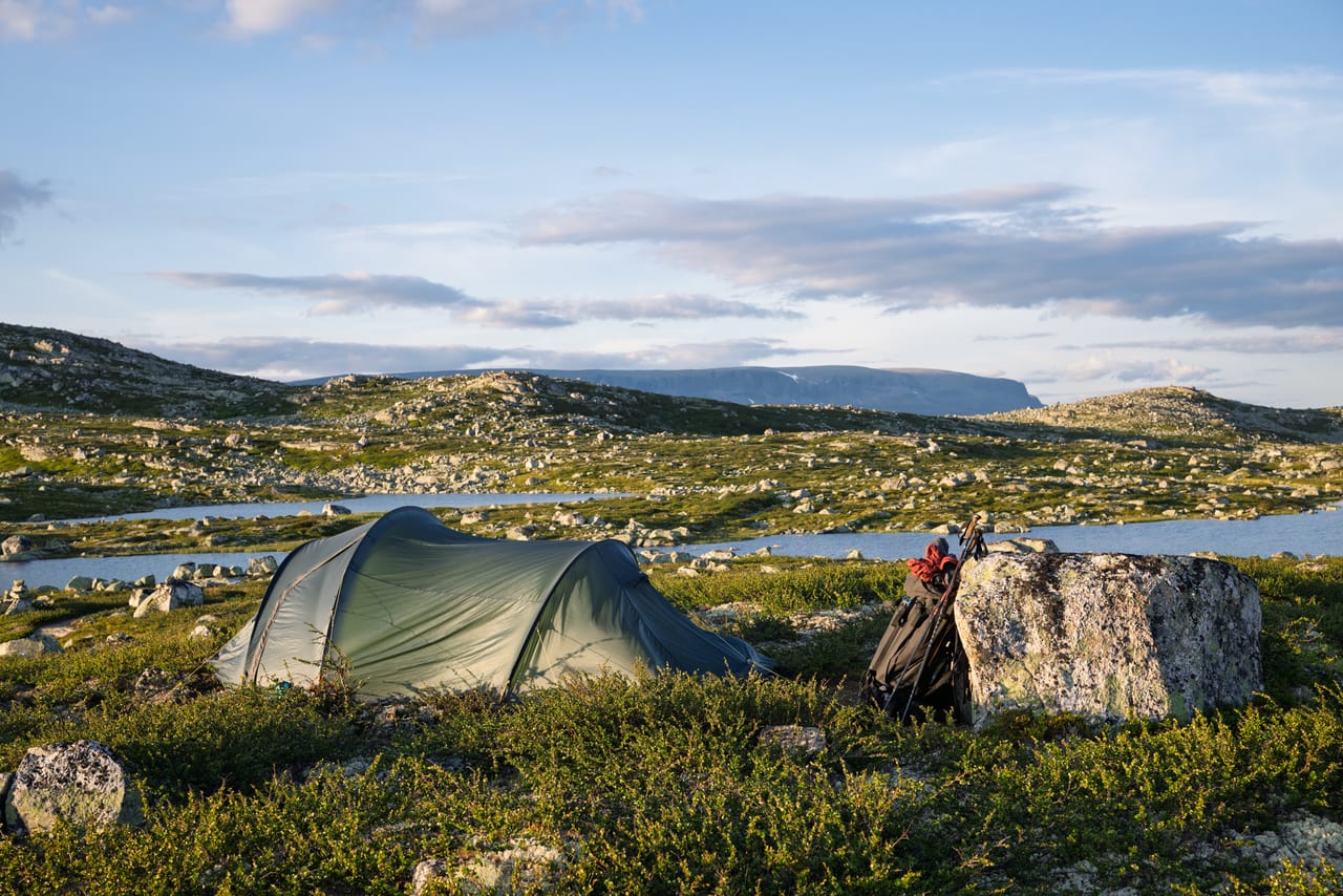 Telt ved Ørteren i kveldslys, med sekk og staver lent mot en stein.